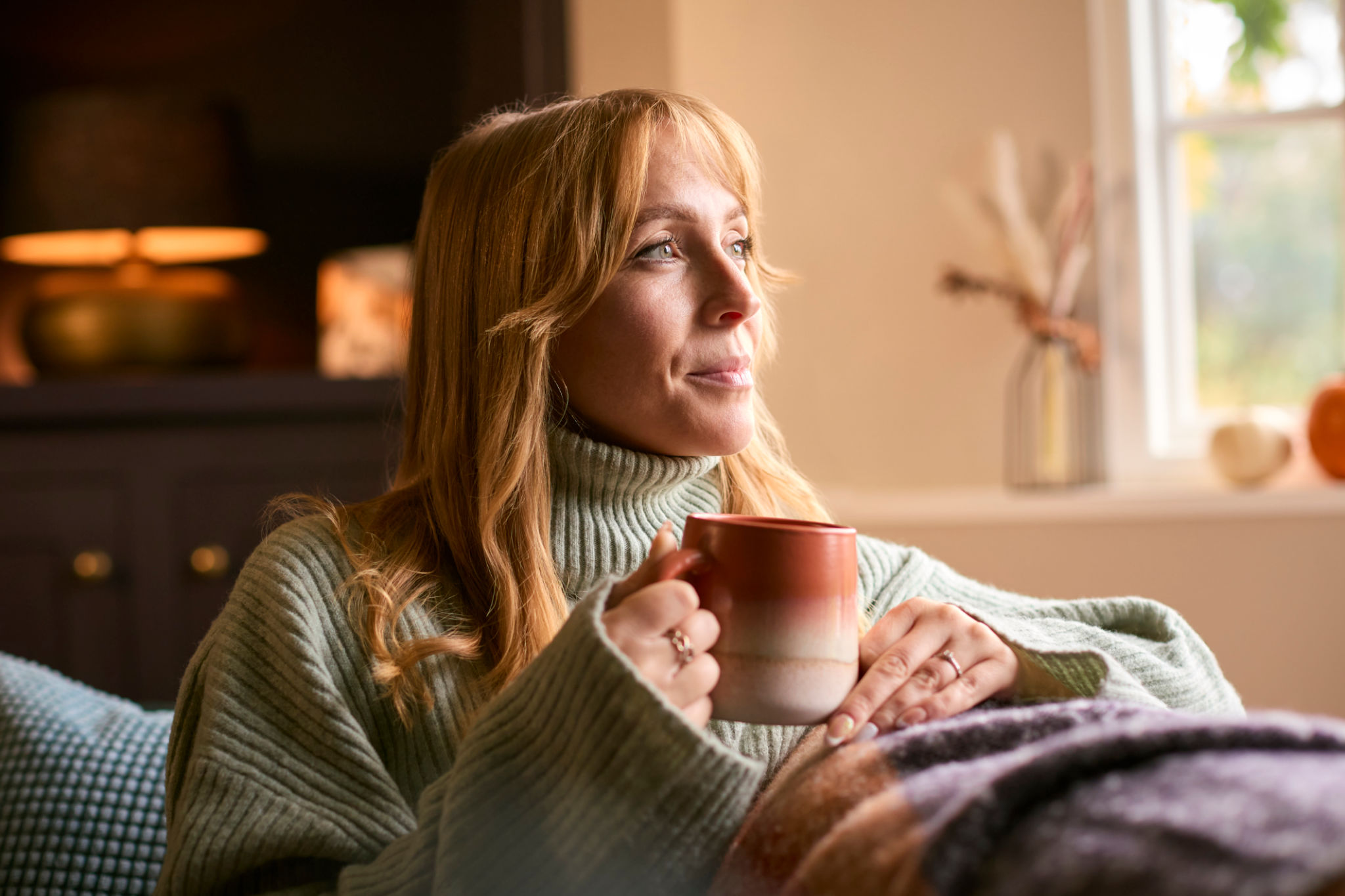 donna over 40 rilassata con tisana serale in casa, luce calda autunnale e atmosfera accogliente
