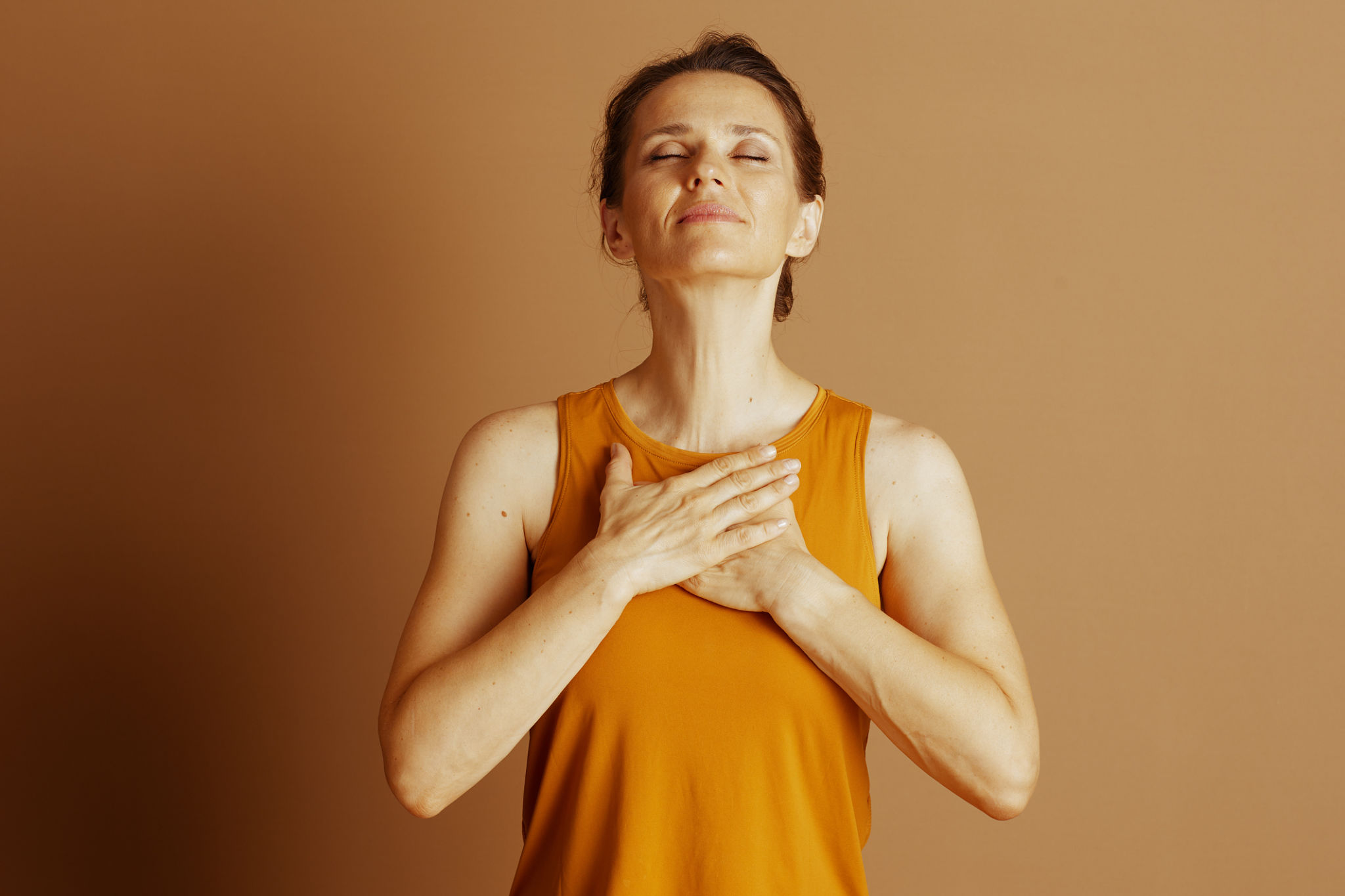 donna over 40 rilassata con mano sul petto, luce naturale beige, simbolo di calma e benessere interiore
