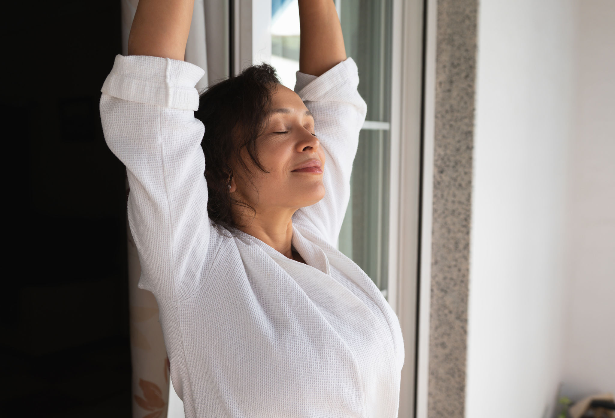 donna over 40 che respira profondamente alla finestra per ridurre il gonfiore addominale