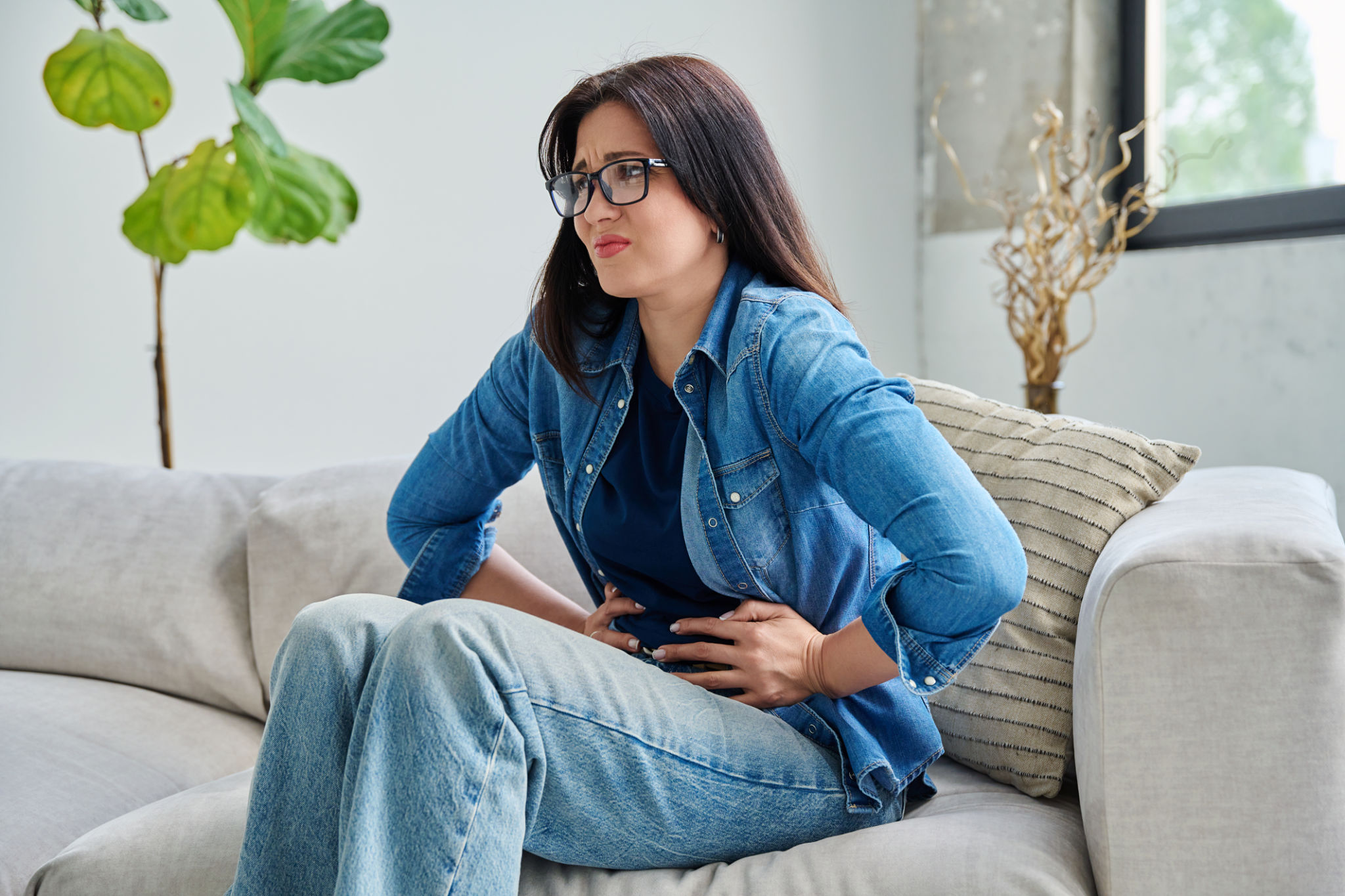bere caffè appena svegli gonfiore con donna seduta sul divano che tiene l’addome