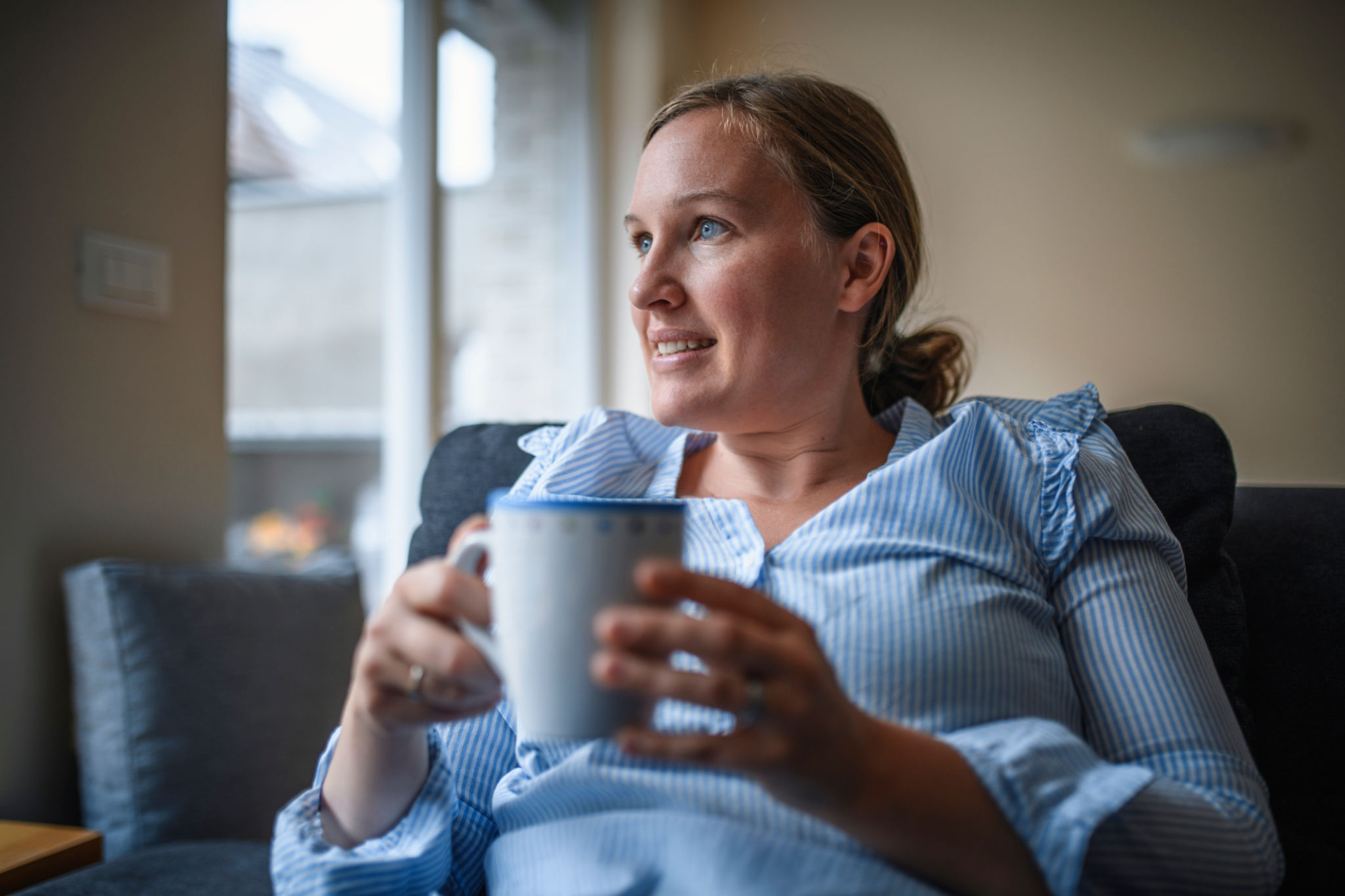 smettere il caffè e gonfiore con donna seduta sul divano che tiene una tazzina al mattino