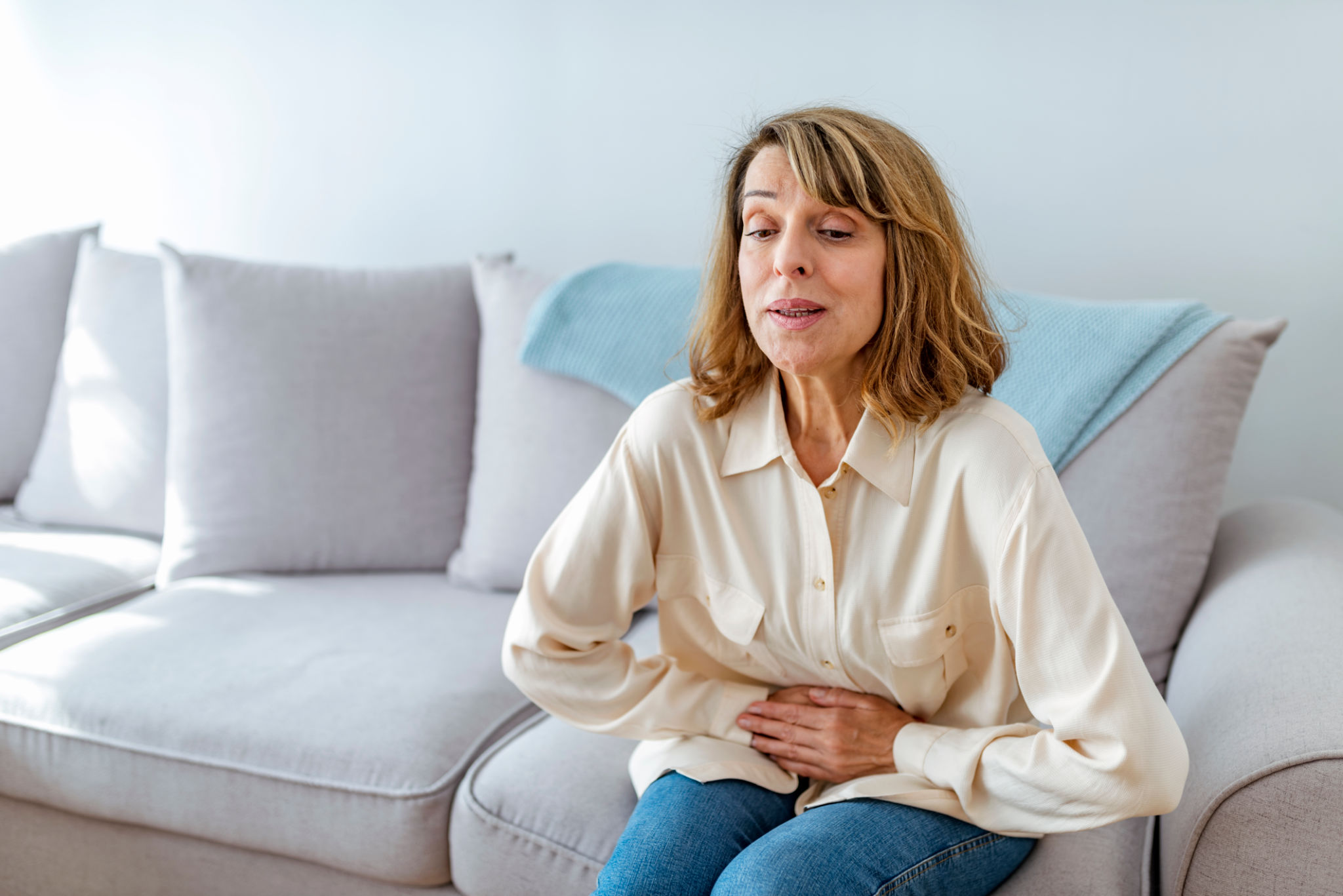 menopausa pancia gonfia dolorante con donna seduta sul divano in casa e fastidio addominale
